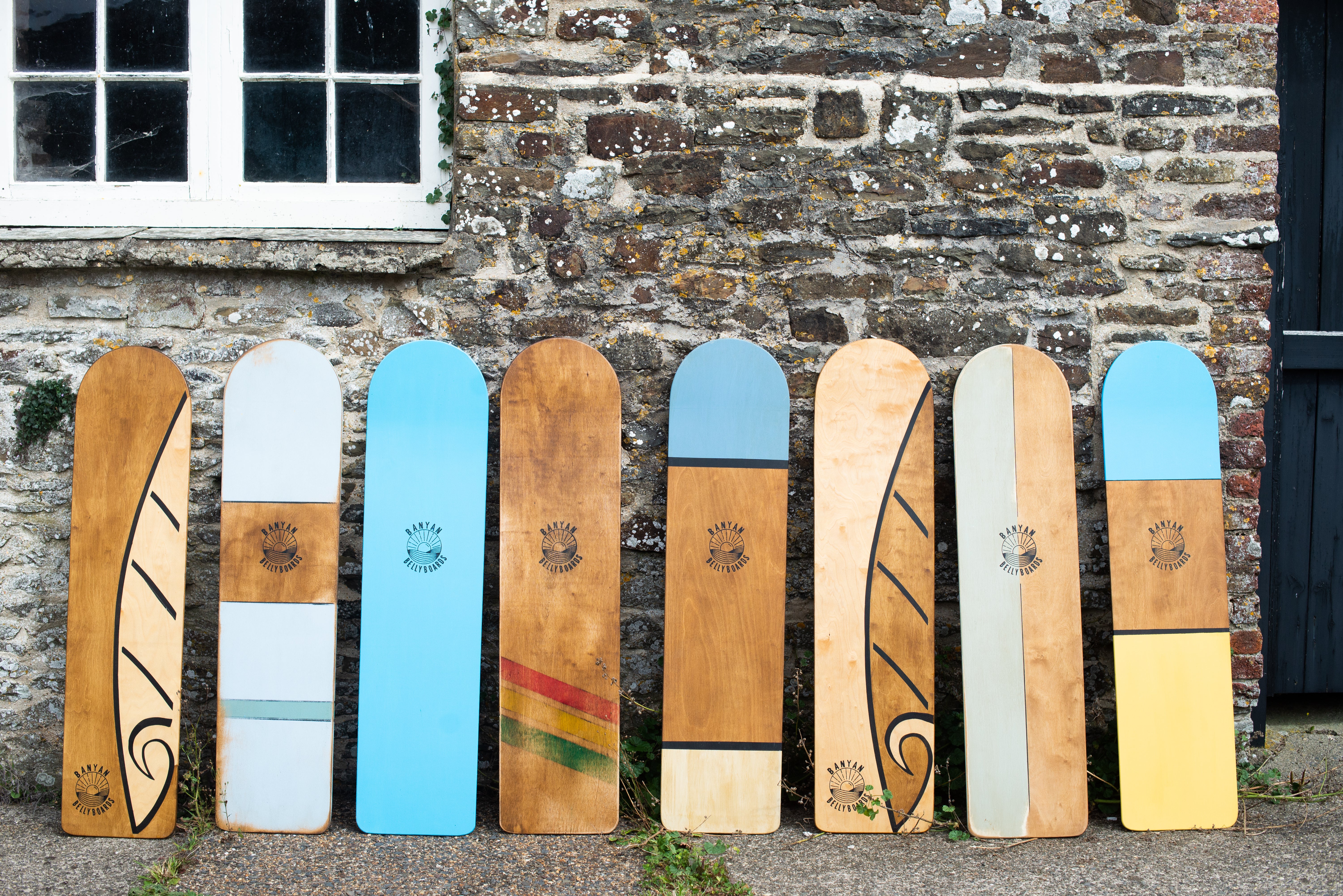 Collection of wooden surfboards with various designs against a stone wall.